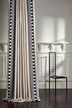 a chair sitting in front of a curtain with black and white striped curtains on it