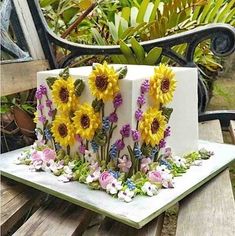 a cake decorated with sunflowers and flowers on a wooden table next to a bench