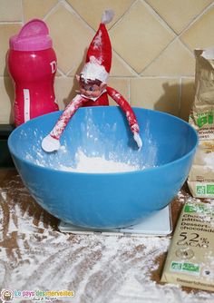 an elf is sitting in a blue bowl with flour on the counter next to it