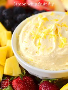 a white bowl filled with lemon whip fruit dip surrounded by sliced bananas and strawberries