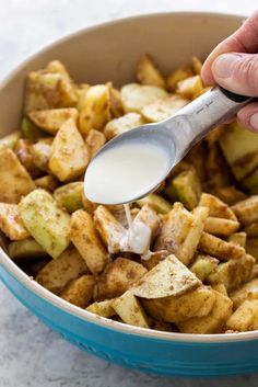 a hand holding a spoon over a bowl filled with potatoes and other foods that are being mixed together