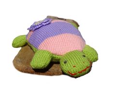 a knitted turtle laying on top of a piece of wood with a pink, purple and green sweater