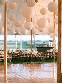 the inside of a large tent with tables and paper lanterns hanging from it's ceiling