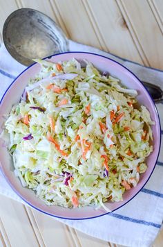 a bowl filled with coleslaw and carrots on top of a white table