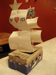 a small wooden boat on top of a table next to a box with paper cutouts