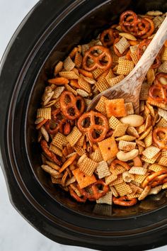 a wooden spoon in a crock pot filled with cheetos and pretzels