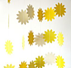 some yellow and white paper flowers hanging from the ceiling in front of a white wall