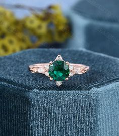 an emerald and diamond ring sitting on top of a blue velvet box with flowers in the background