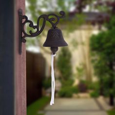 a bell hanging from the side of a building next to a sidewalk with trees in the background