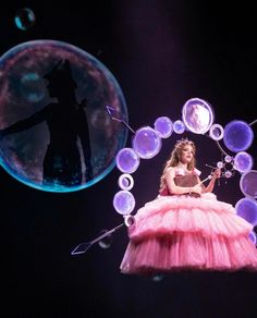 a woman in a pink dress on stage with bubbles around her and a silhouette of a man