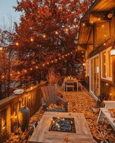 an outdoor deck with lights strung from the ceiling and chairs on it, surrounded by fall leaves