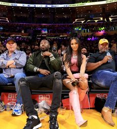 three people sitting in the stands at a basketball game, one is holding a microphone