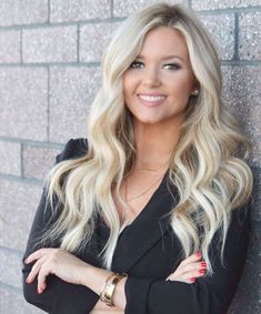 a woman with long blonde hair standing in front of a brick wall wearing a black blazer