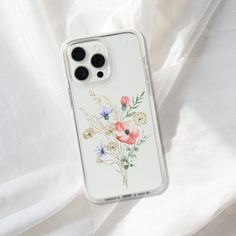 an iphone case with flowers painted on it sitting on a white sheet covered bedding