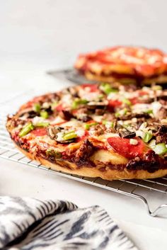 two pizzas sitting on top of a cooling rack next to each other in front of a white table