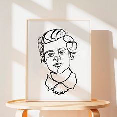 a black and white drawing of a woman's face on a wooden shelf next to a window