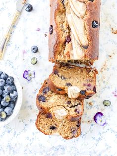 sliced loaf of blueberry banana bread next to bowl of fresh blueberries