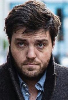 a close up of a person wearing a jacket and looking at the camera with a serious look on his face