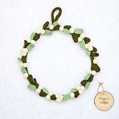 a green and white beaded bracelet with a gold charm on the clasp that says paper high