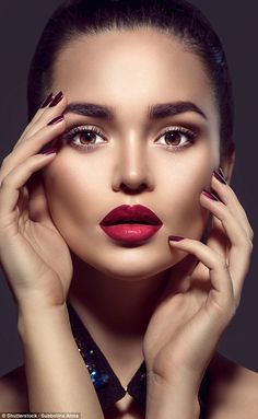 a woman with red lipstick and dark nails holding her hands to her face while posing for the camera