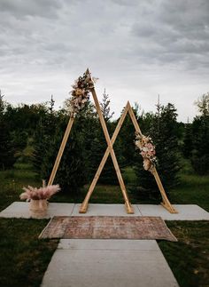 a wooden triangle with flowers on it sitting in the middle of a field next to trees