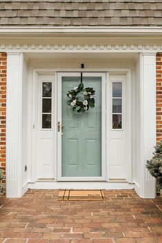 a white front door with a green wreath on it's side and brick walkway