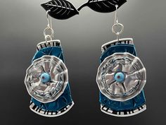 a pair of blue and silver earrings with leaves hanging from the back of them,