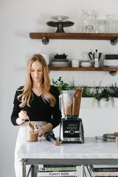 a woman standing in front of a blender filled with liquid and coffee making it