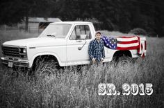 a man standing next to a white truck with an american flag on the bed in a field