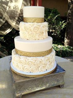 a three tiered white and gold wedding cake sitting on top of a silver tray