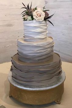 a three tiered wedding cake with white flowers on the top and gray ribbons around it