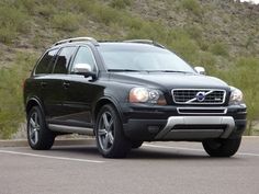 a black volvo suv parked in a parking lot next to a hill side with grass and bushes