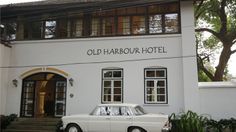 an old fashioned car parked in front of a white building with black windows and the words old harbour hotel written on it