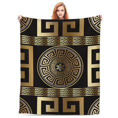 a woman holding up a black and gold blanket with an intricate design on the front