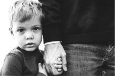 a black and white photo of a young boy holding the hand of an adult's hand