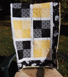 a black and yellow quilt sitting on top of a wooden chair next to a tree