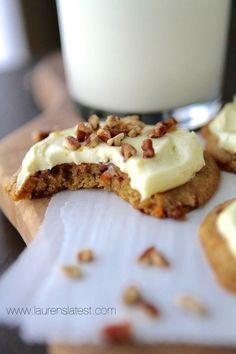 some cookies with white frosting and nuts are on a table next to a glass of milk