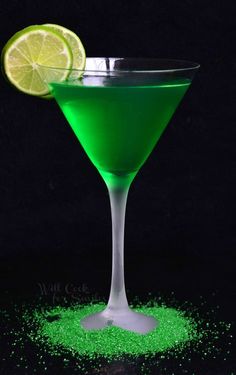 a green drink in a martini glass with a lime slice on the rim and sprinkles around it