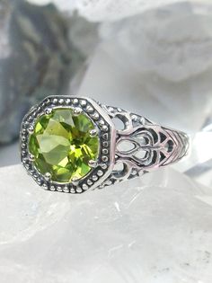 Natural Peridot RingNew Vic Design#D11 Inspired by Victorian and Edwardian designs, this stunning antique reproduction ring is crafted in white gold. This gorgeous ring is set with a flawless round natural peridot. The stunning gemstone is 8mm in diameter. The band is marked 925 (sterling silver),10k or 14k as chosen. Notice the beautifully intricate design of the silver filigree setting and band. The delicate swirl filigree craftsmanship travels down the band and morphs into angular accents. The stunning gem sits in the center of a silver frame that highlights its shape and brilliance. Its border of delicate balls and ridges surrounding the gemstone serve to give a softer, lighter look. The ornate filigree flows all the way down the side of the band in a gentle fashion. This ring speaks o Classic Peridot Jewelry For May Birthstone, Antique Green Promise Ring, Classic Peridot Jewelry With Accent Stones, Green Gemstone Filigree Ring For May Birthstone, Green Gemstone Filigree Ring, Classic Green Filigree Ring With Gemstone, Classic Peridot Ring Jewelry, Green Filigree Ring For May Birthstone, Vintage Peridot Ring For May Birthstone