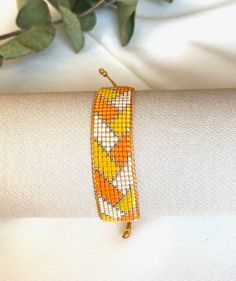 an orange and yellow beaded bracelet sitting on top of a white cloth next to a plant