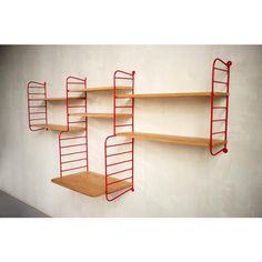 three wooden shelves with red metal shelving on the wall next to eachother