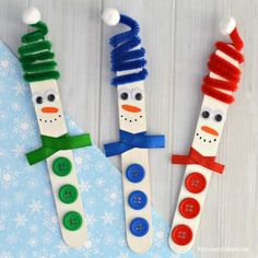 three snowmen made out of popsicle sticks with buttons on them and one is wearing a scarf