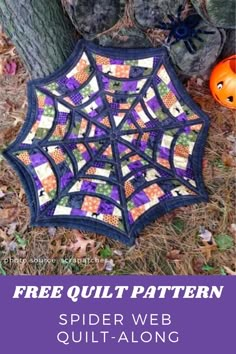 a spider web quilt on the ground next to a tree with pumpkins in it