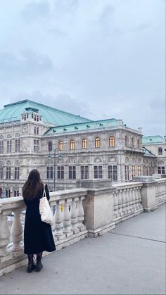 a woman is standing on a bridge looking at the building in the distance with her purse