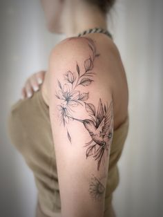 a woman's arm with flowers on it and a bird flying over the top