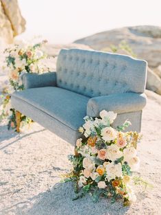 a blue couch sitting on top of a sandy beach next to a bouquet of flowers