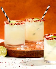 two margaritas sitting on top of a wooden cutting board