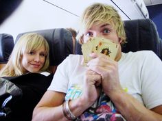 a man sitting next to a woman on top of an airplane while holding up cards