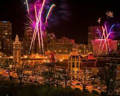 fireworks are lit up in the night sky over a city skyline with buildings and trees