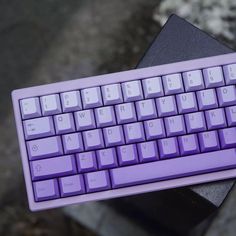 a purple computer keyboard sitting on top of a black table next to a stone wall